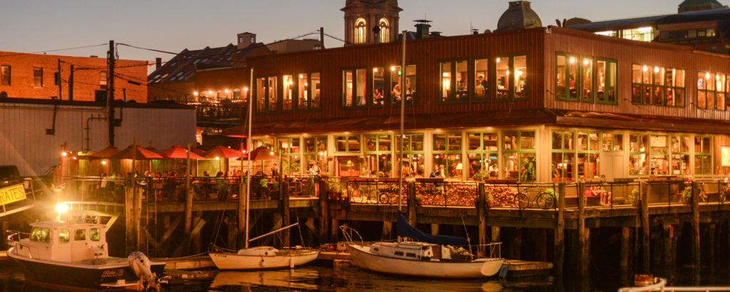 outdoor nighttime shot of portland maine waterfront with outdoor dining and boats out front