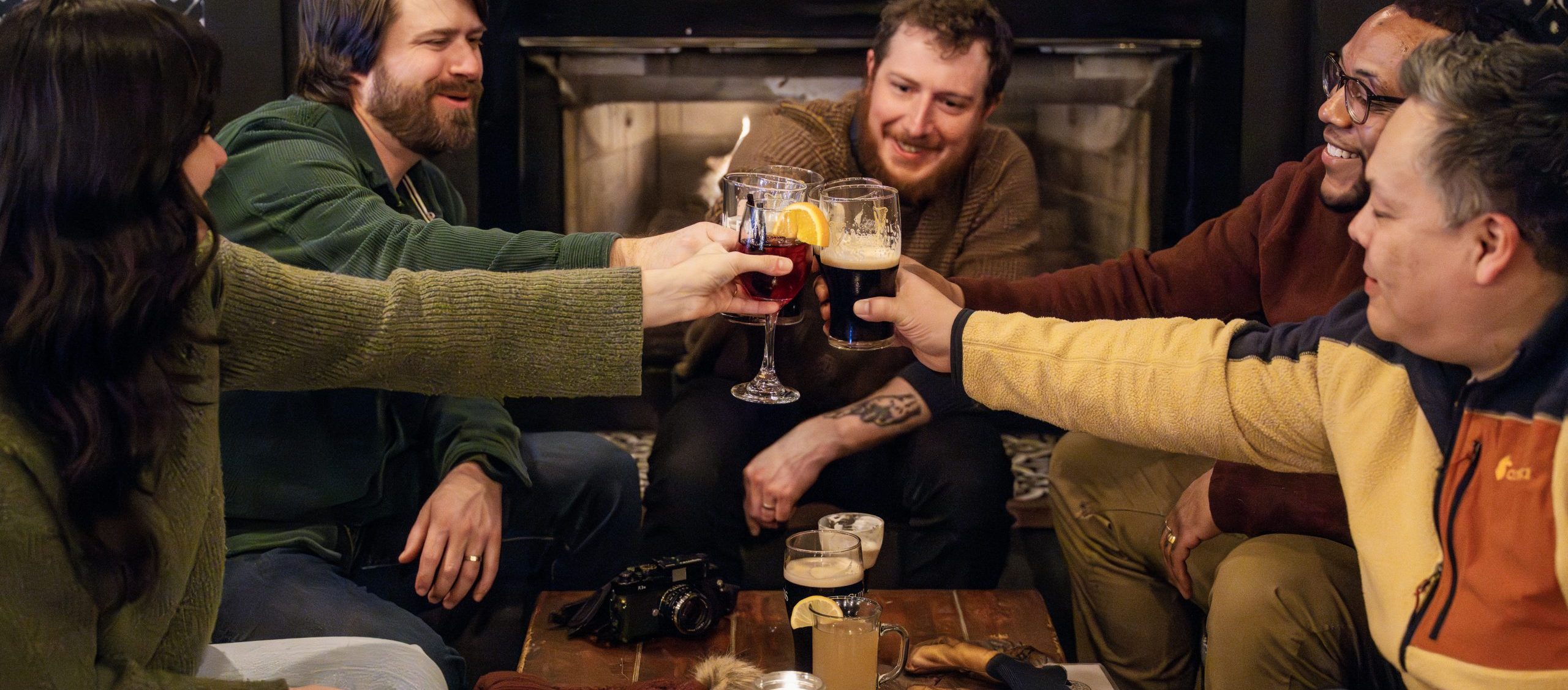 A group of friends toasting with drinks in front of a cozy fireplace in Portland Maine.