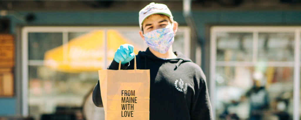 Man in mask and gloves holding bag saying 'from Maine with love', Photo Courtesy of Mat Trogner, via Allagash Brewing