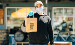 Man in mask and gloves holding bag saying 'from Maine with love', Photo Courtesy of Mat Trogner, via Allagash Brewing