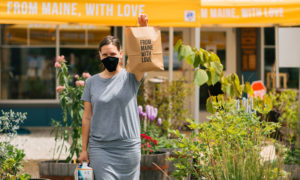 Woman holding up bag saying 'from Maine with love' while wearing mask, Photo Courtesy of Mat Trogner, via Allagash Brewing