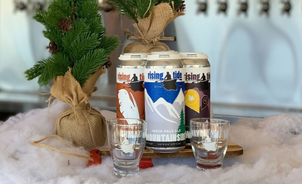 Beer Cans Lined-up in Front of a Holiday Tree, Photo Credit: Rising Tide Brewery Beer Cans Lined-up in Front of a Holiday Tree, Photo Credit: Rising Tide Brewery