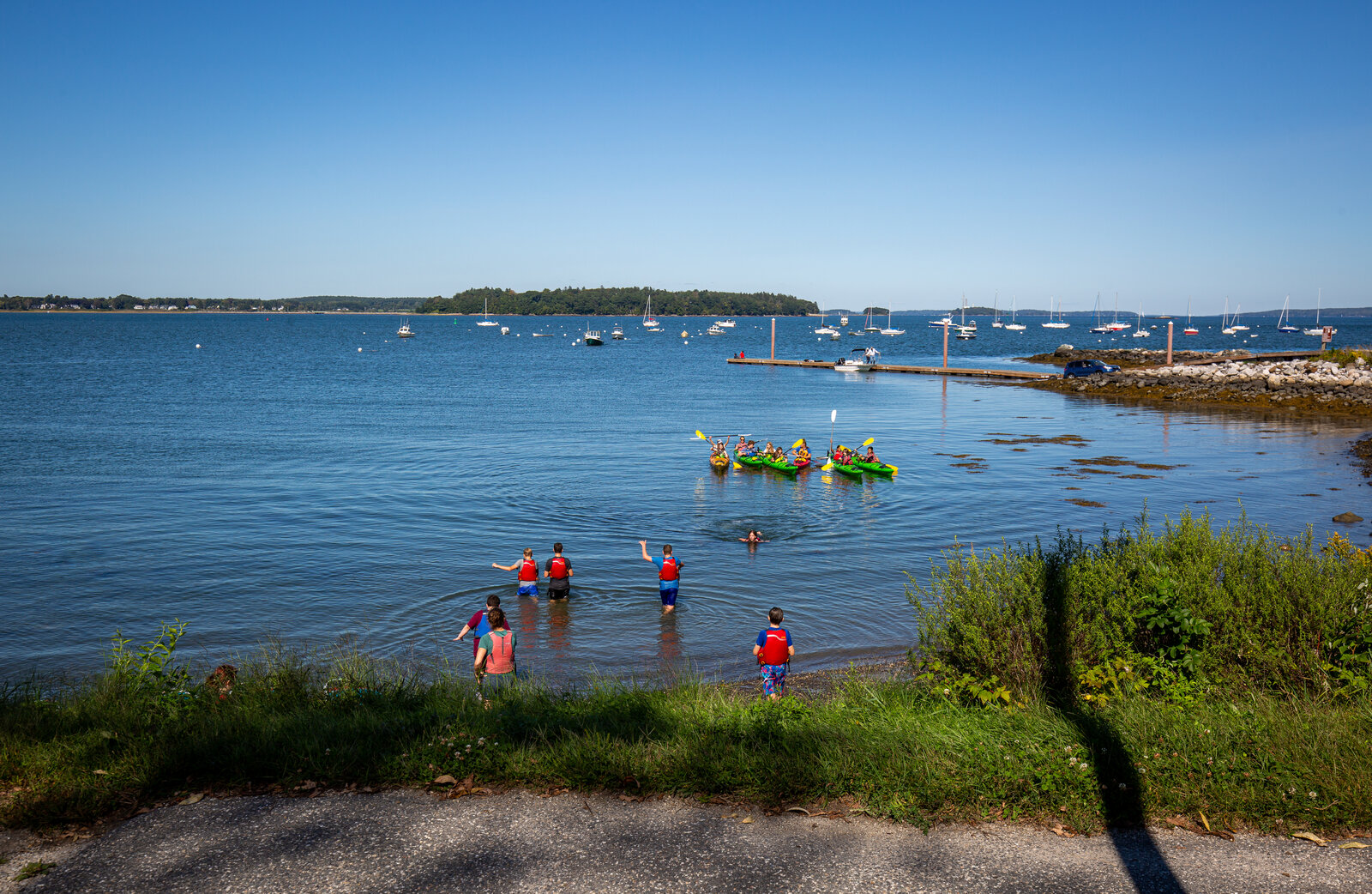 People in life jackets enter the water near a group of kayakers in a bay in Portland Maine.