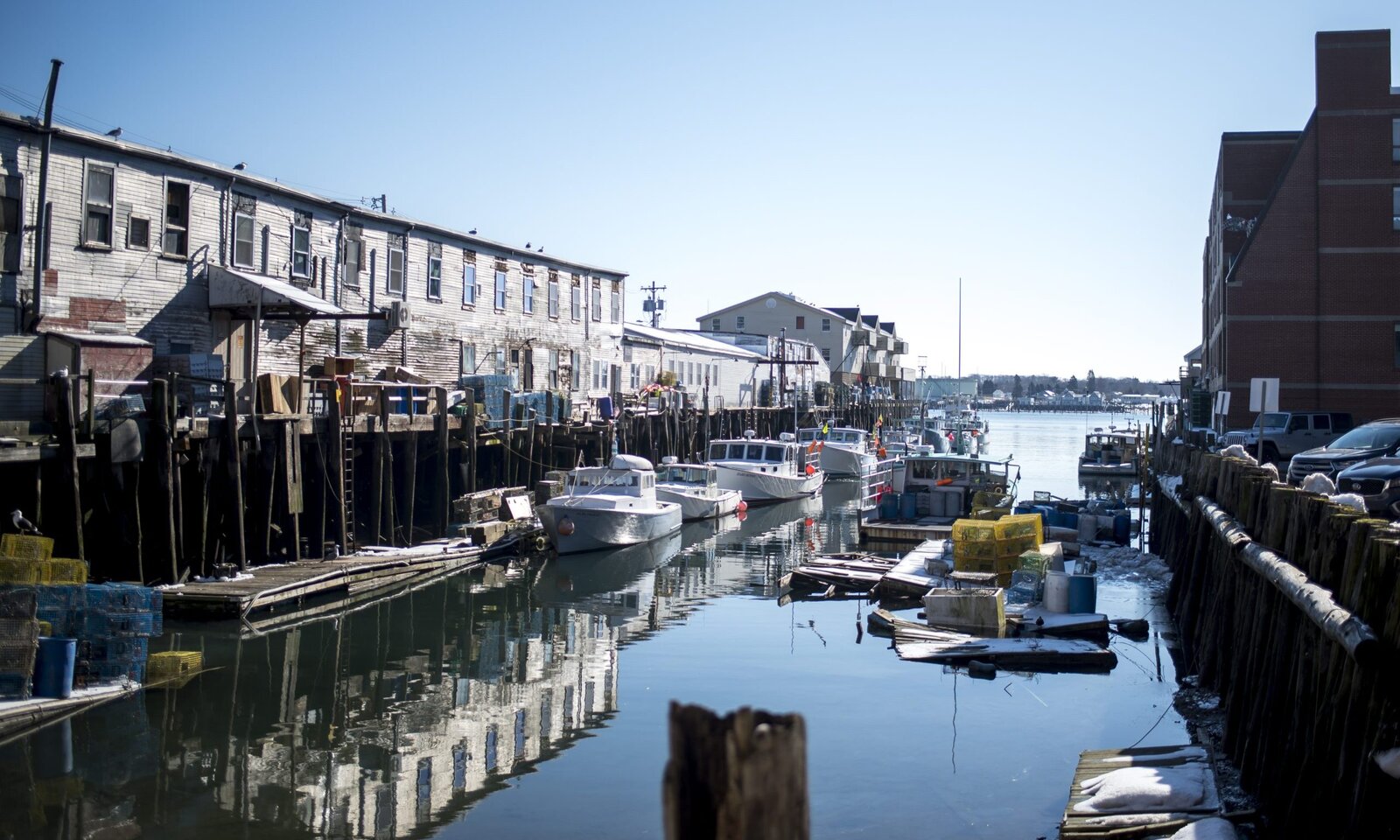 Fishing boats docked in a narrow harbor lined with weathered wooden buildings in Portland Maine.