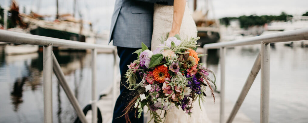 A bride and groom standing on a dock at the Camden Harbor. Photo Credit: Lindsay Vann Photography