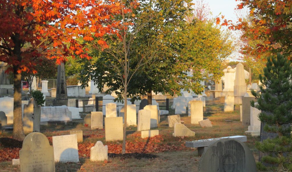 A peaceful cemetery filled with old gravestones surrounded by colorful autumn trees in Portland Maine.