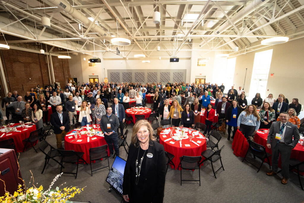 A large group of people attending a conference in a spacious, high-ceilinged event hall in Portland Maine.