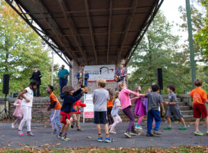 A group of children dancing outdoors while a band performs on a stage in Portland Maine.