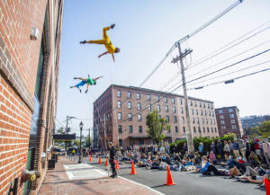 Two acrobats perform a high-flying stunt in the air above a crowd in Portland Maine.