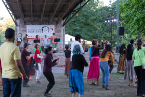 A group of people dancing outdoors in front of a stage under a bridge in Portland Maine.
