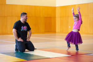 A man watches a young girl in a tutu practicing gymnastics on a mat in Portland Maine.