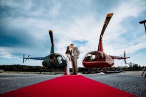Couple in front of Helicopters. Photo Credit: Pine Tree Helicopters