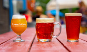 Lineup of different orange and red beers on red picnic table; Photo Credit: Peter G. Morneau Photography