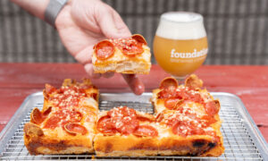 Hand grabbing peperoni pizza and beer on red picnic table ; Photo Credit: Peter G. Morneau Photography