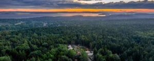 Aerial of yurt community surrounded by green woods and ocean at sunset; Photo Credit: Peter G. Morneau Photography