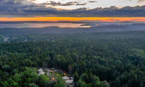 Aerial of yurt community surrounded by green woods and ocean at sunset; Photo Credit: Peter G. Morneau Photography