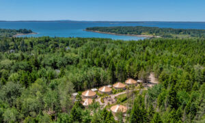 Aerial of yurts surrounded by green forest and blue ocean; Photo Credit: Peter G. Morneau Photography