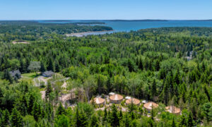 Aerial of yurt community surrounded by green forest and ocean; Photo Credit: Peter G. Morneau Photography
