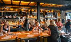 People socializing at wooden table at bar; Photo Credit: Lauren Peters at Visit Portland