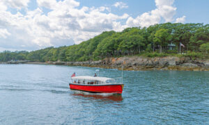 red boat sailing past green island on blue water; Photo Credit: Peter G. Morneau Photography