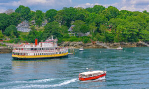 red boat sailing past rocky island and yellow ferry boat on blue water; Photo Credit: Peter G. Morneau Photography