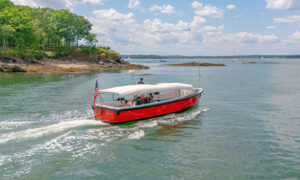 Red boat sailing past island on blue water; Photo Credit: Peter G. Morneau Photography