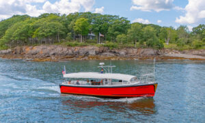 red boat sailing past rocky island on blue water; Photo Credit: Peter G. Morneau Photography
