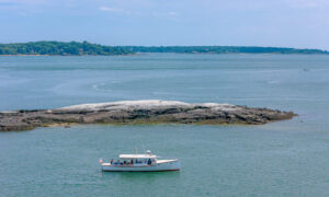 Boat sailing past rocky island on blue water; Photo Credit: Peter G. Morneau Photography