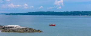 Boat sailing past rocky island on blue water; Photo Credit: Peter G. Morneau Photography