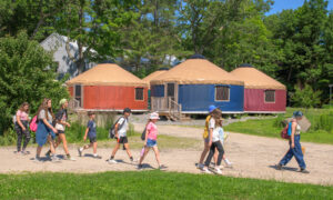 The Ecology School orange yurts with group walking; Photo Credit: Peter G. Morneau Photography