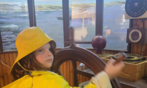 Little girl playing with wooden ship steering: Photo Credit: Maine Maritime Museum