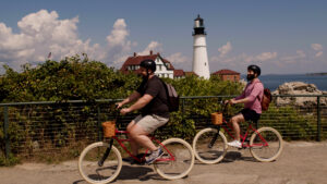 Couple on bikes in front of Portland Head Light, Photo Credit: Knack Factory