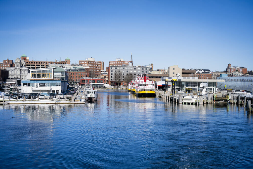 A harbor with docked boats and buildings under a clear blue sky in Portland Maine.