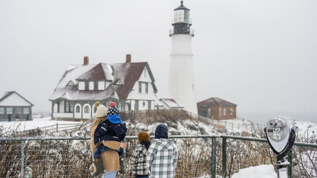 A family looks at a lighthouse during a snowy winter day in Portland Maine.