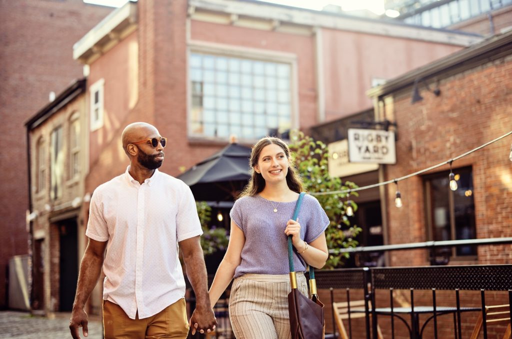 A diverse couple holding hands while walking through a brick-lined urban courtyard in Portland Maine.