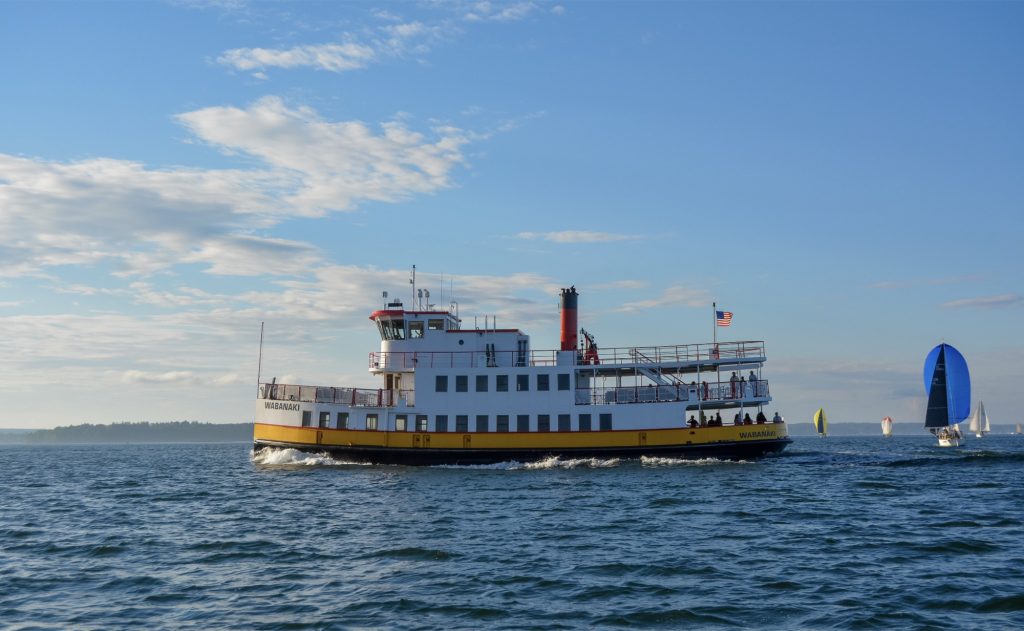 A ferry named Wabanaki travels across the water with sailboats in the distance in Portland Maine.