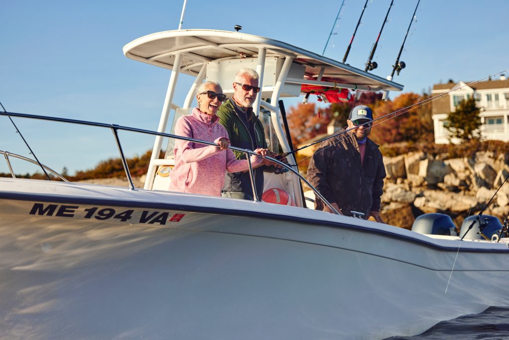 Three people smiling while fishing from a boat on a sunny day in Portland Maine.