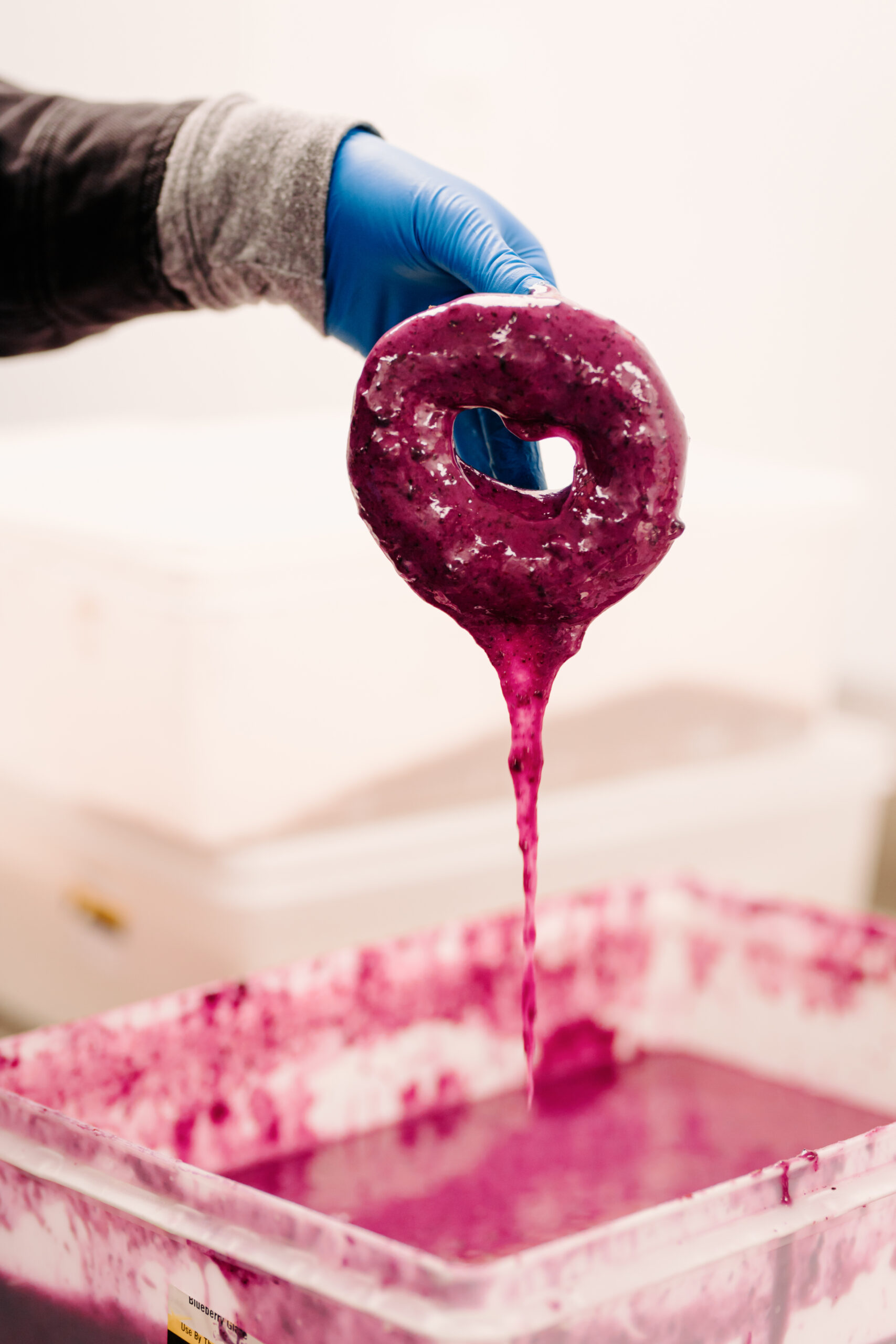 A gloved hand dips a donut into a container of purple blueberry glaze in Portland Maine.