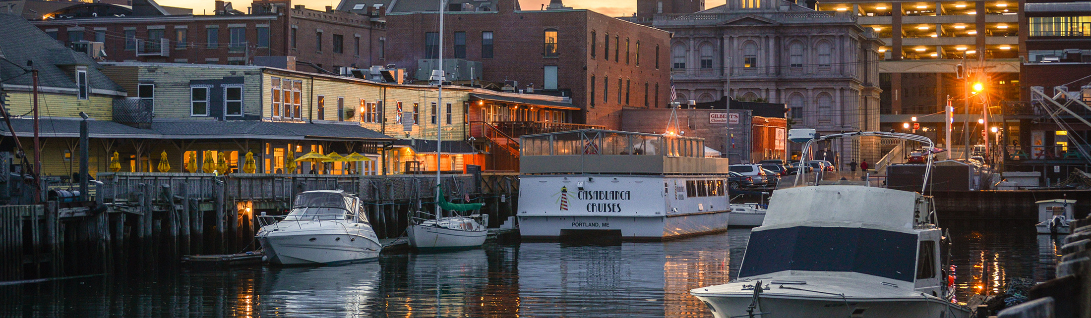 Boats docked at a harbor in front of buildings during sunset in Portland Maine.