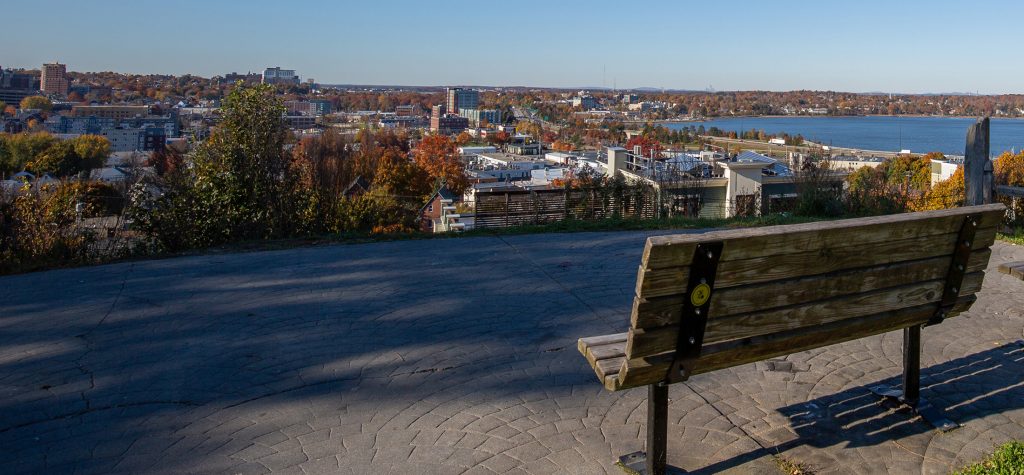 A wooden park bench overlooks a city skyline and a body of water in Portland Maine.