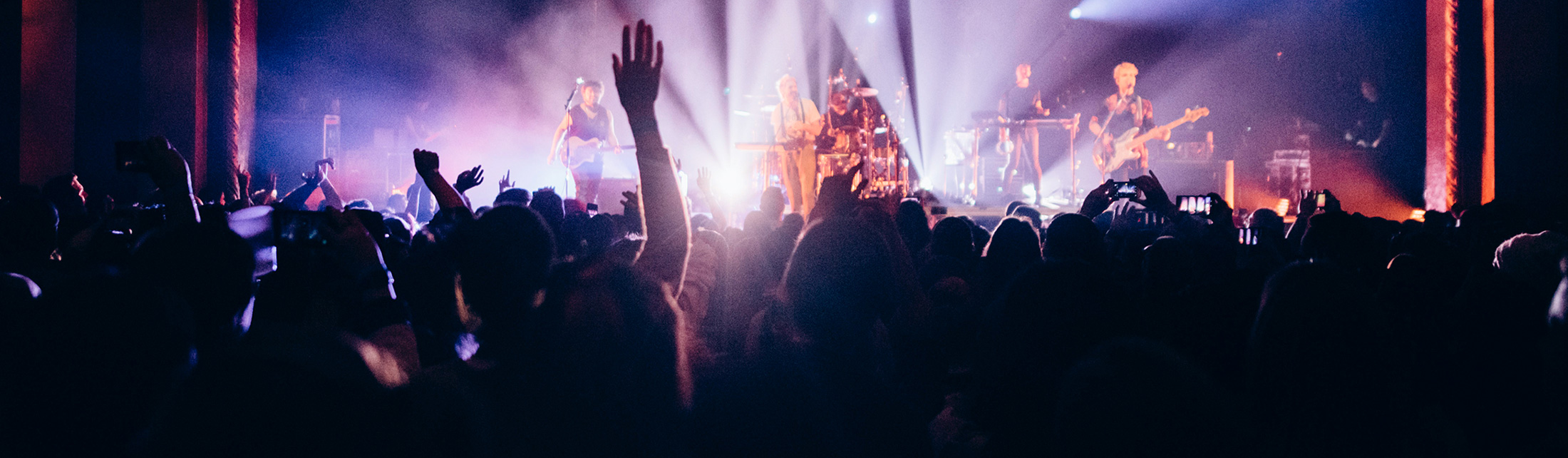 A crowd of people watching a band perform on a brightly lit stage in Portland Maine.