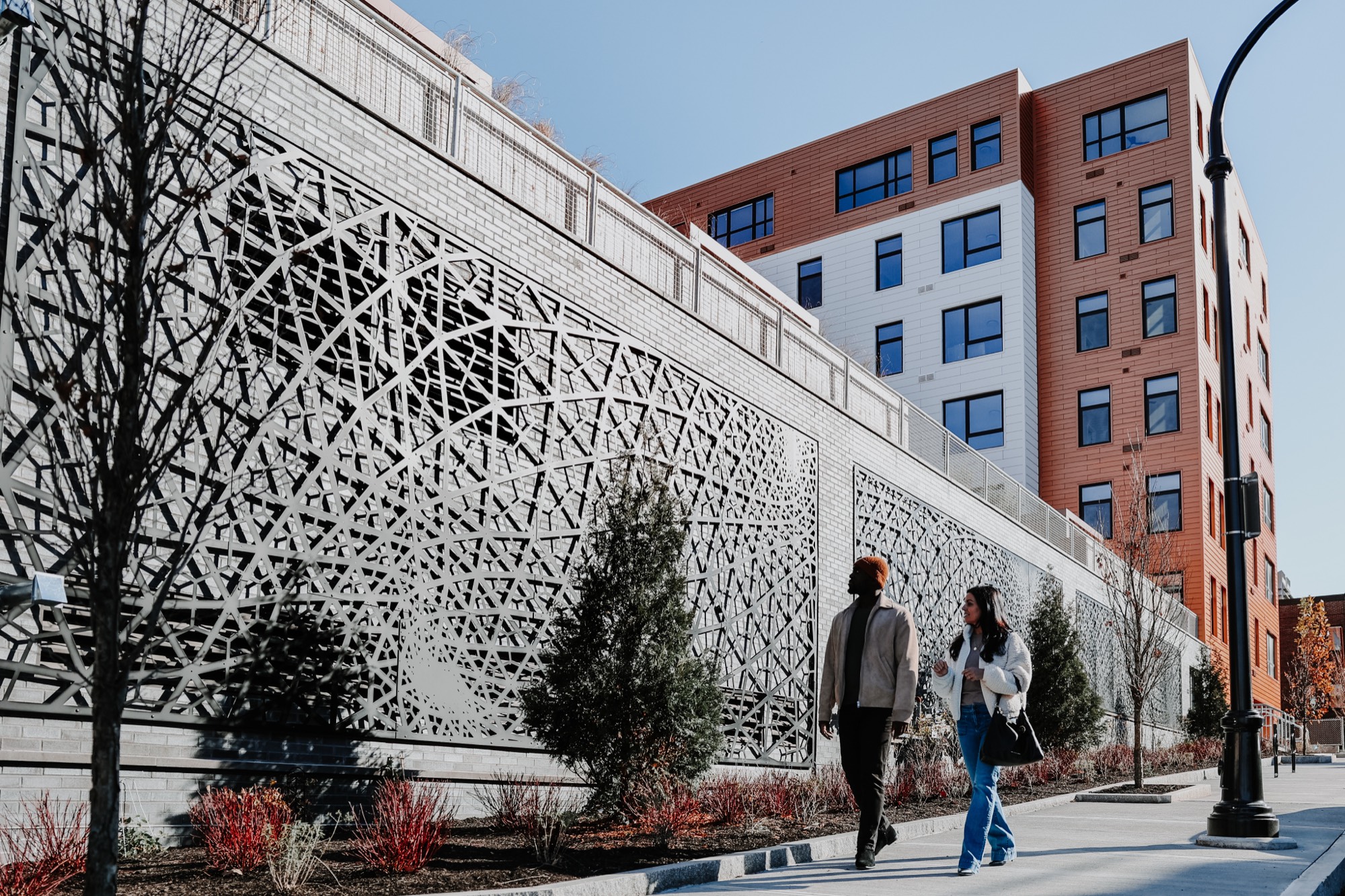A man and woman walking together on a sidewalk beside a modern patterned wall in Portland Maine.