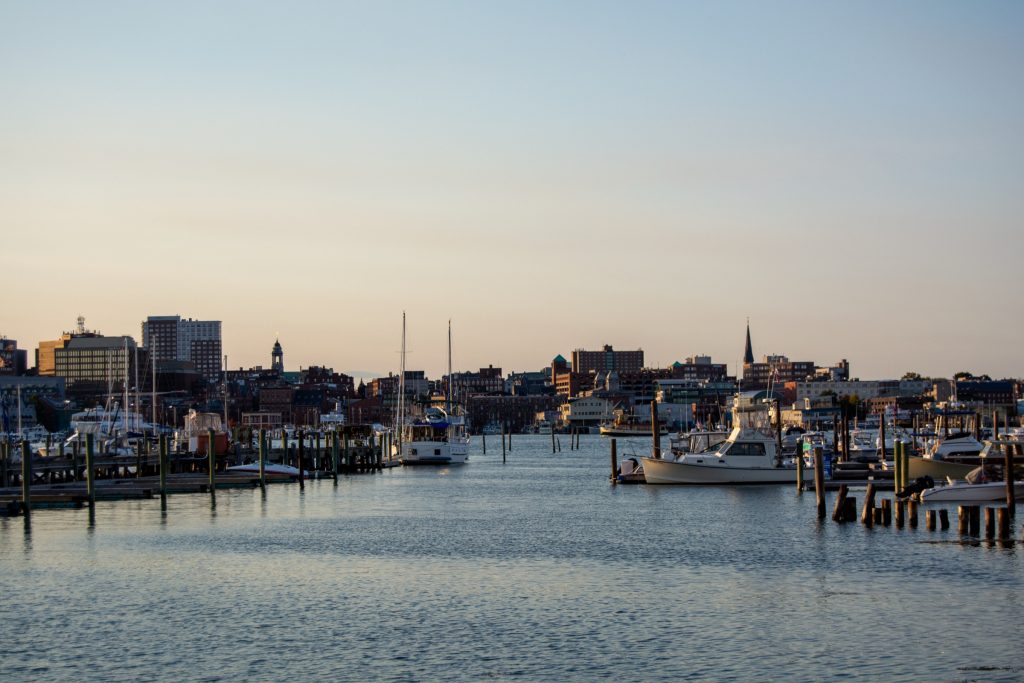 Boats docked in a harbor with a city skyline in the background at sunset in Portland Maine.