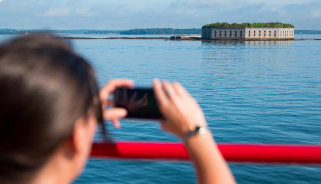 A person takes a photo of an old stone fort in the middle of water in Portland Maine.