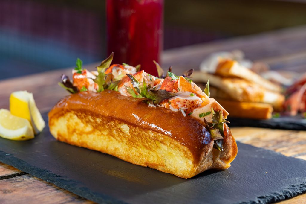 A delicious lobster roll served on a slate board with lemon wedges in Portland Maine.