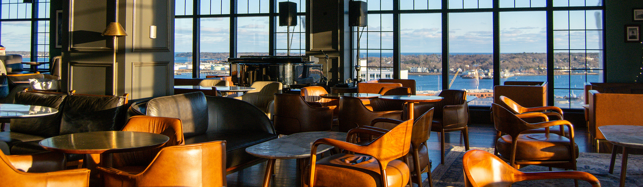 A sophisticated lounge with leather chairs and tables overlooking a harbor at sunset in Portland Maine.