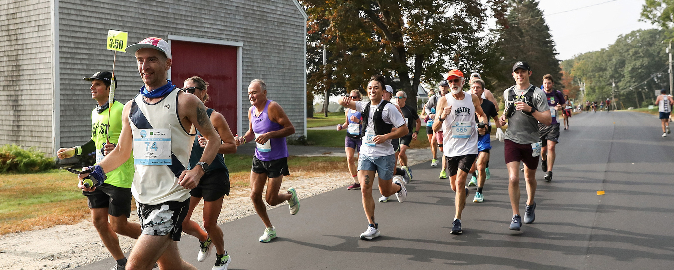 A group of runners participating in a road race on a sunny day in Portland Maine.