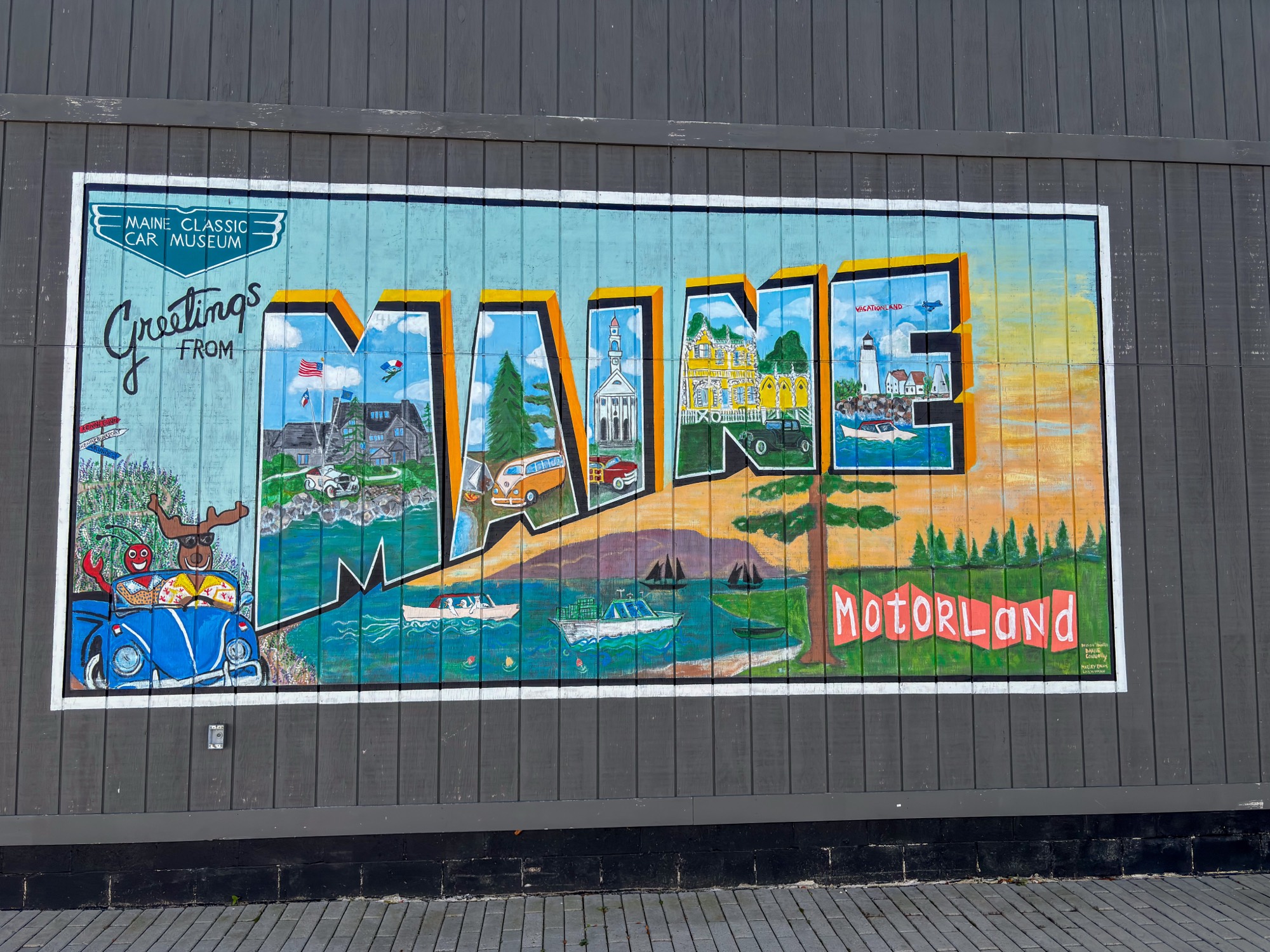 A colorful mural depicting Maine landmarks and a classic car on a wooden wall in Portland Maine.