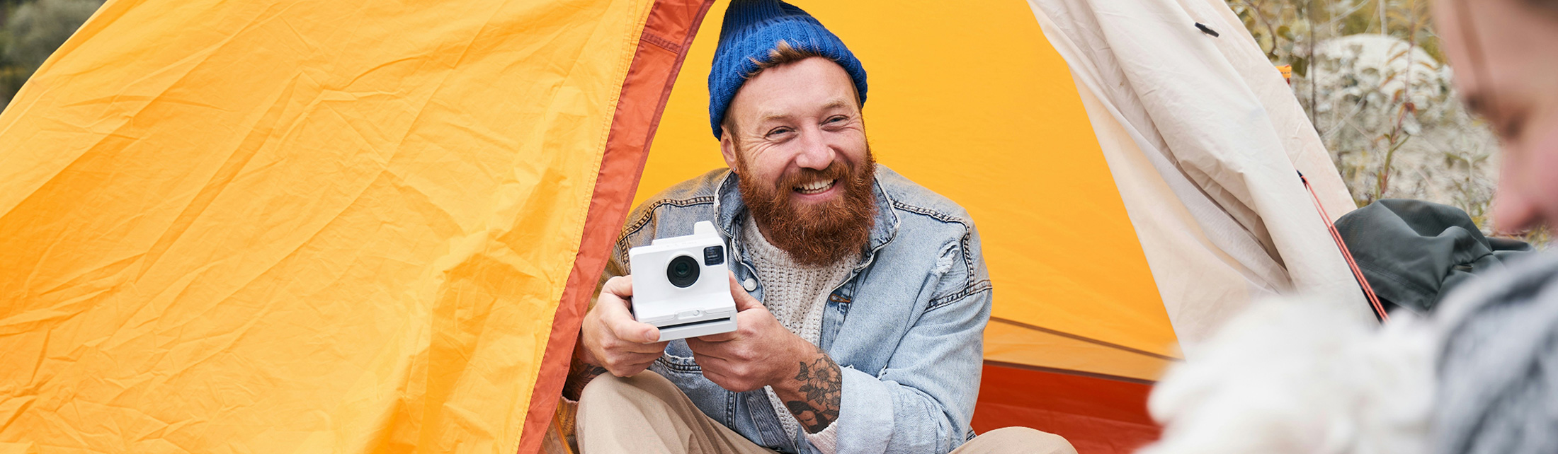 A smiling man with a beard holds a camera inside a yellow camping tent in Portland Maine.