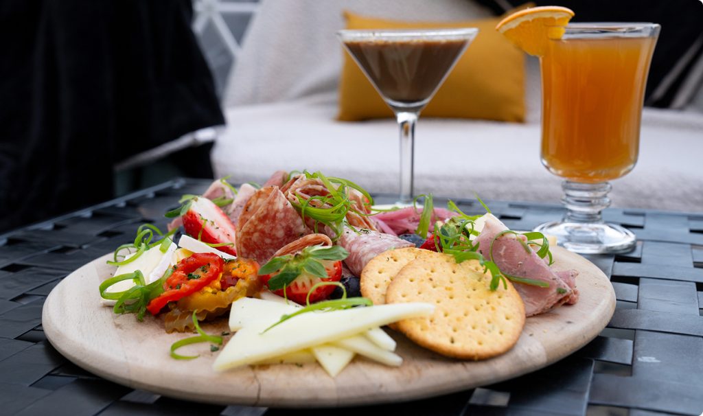 A charcuterie board with meats, cheeses, crackers, and fruit served with two cocktails in Portland Maine.